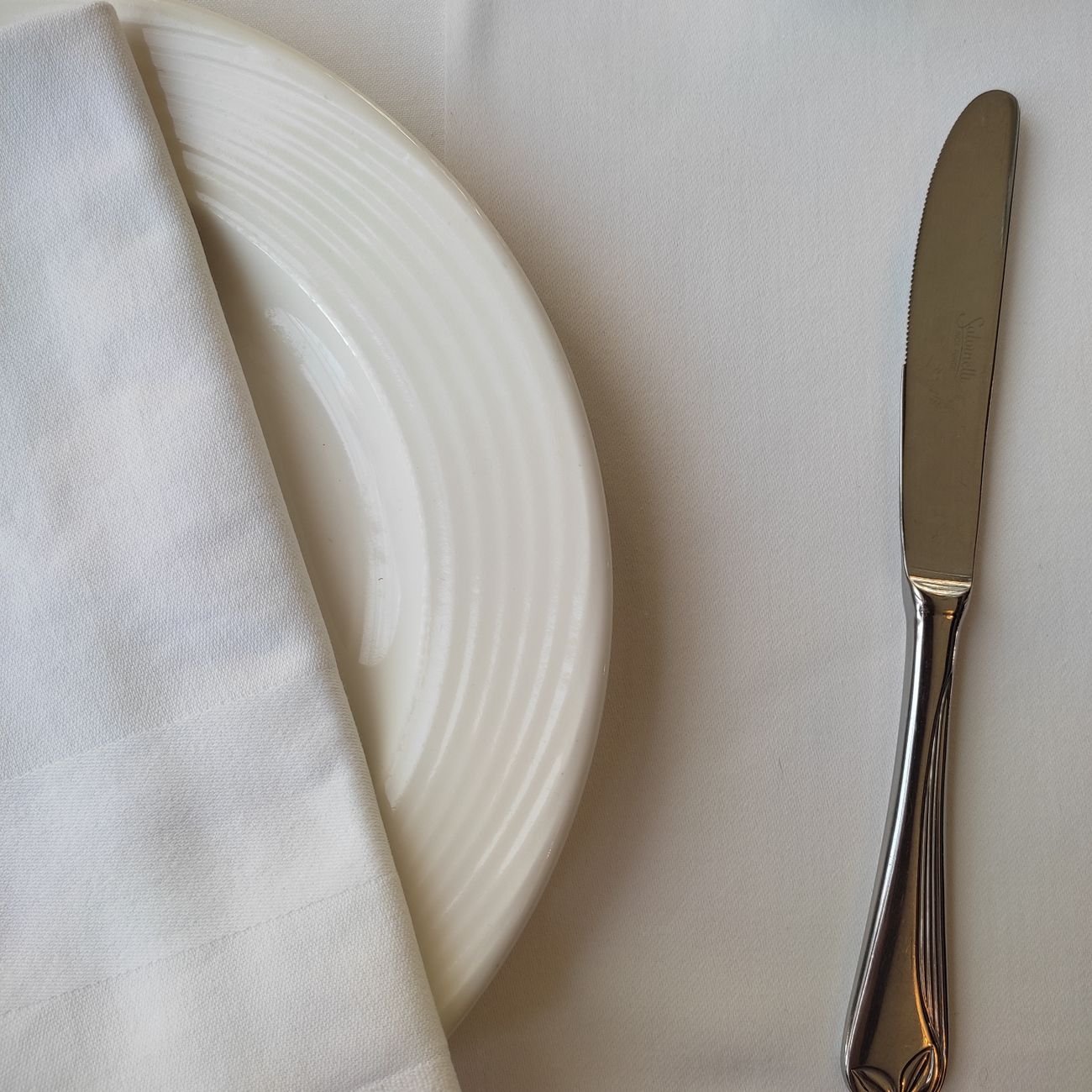 Classic table setting with ceramic plate, knife, and napkin on white cloth