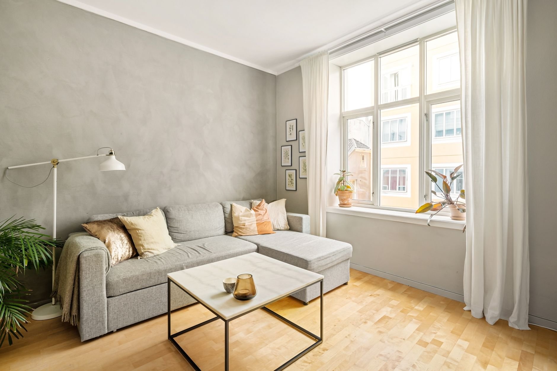 A bright and cozy modern living room featuring a gray sofa and large window for natural light