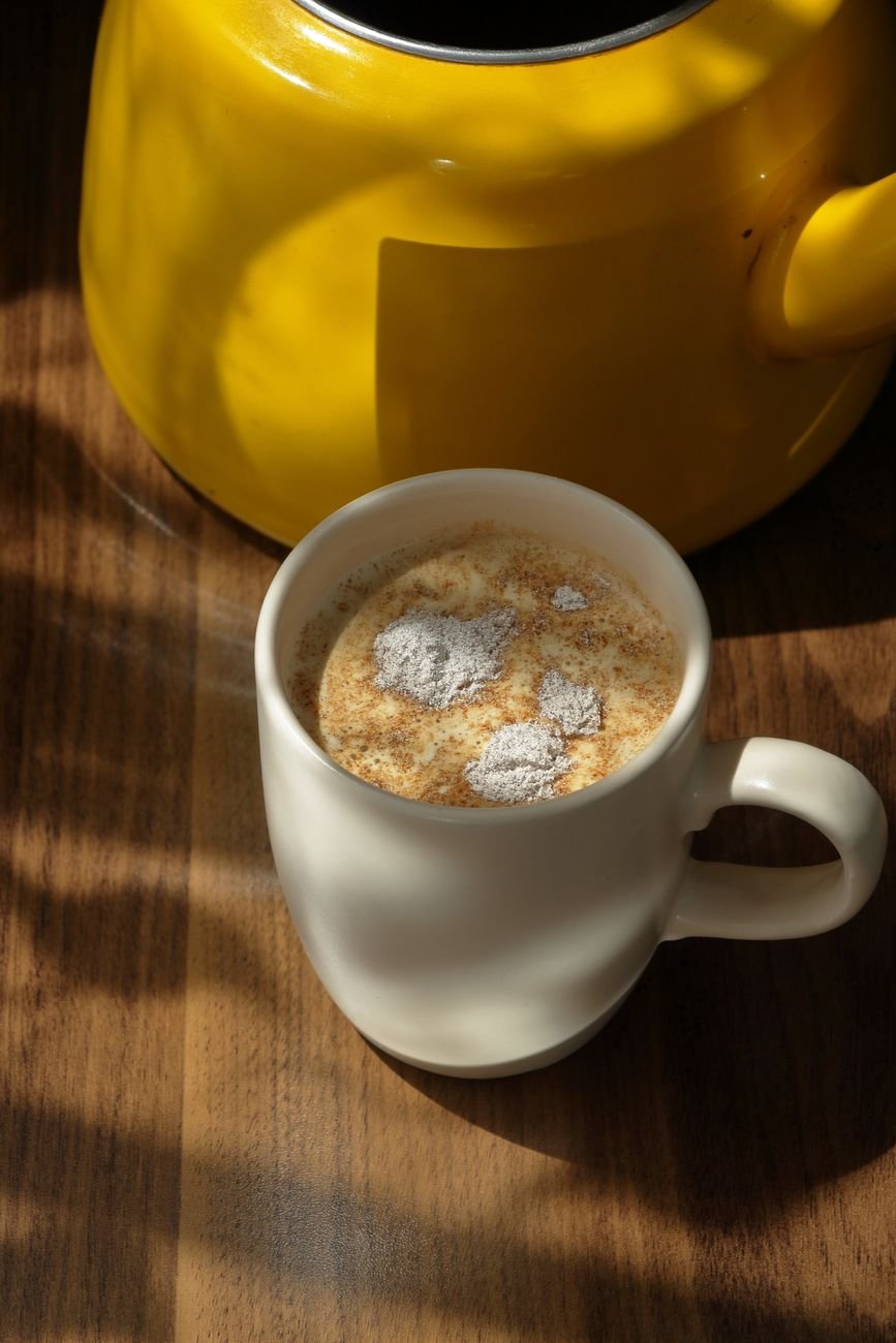 A warm beverage in a ceramic mug under sunlight with a yellow teapot