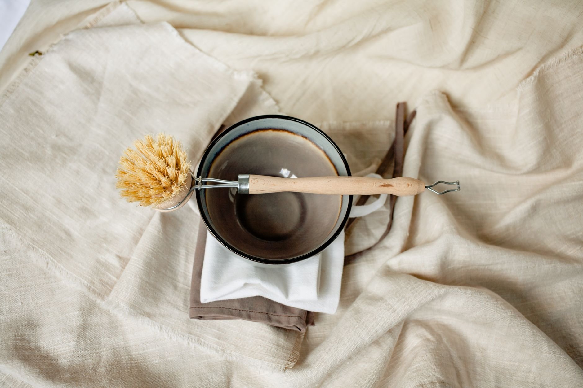 Eco-friendly wooden brush and ceramic bowl on linen fabric — a rustic kitchen scene